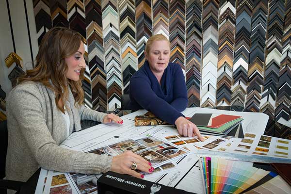 Artifex designer and interior decorator looking at artwork commissions, with color samples spread out across a table